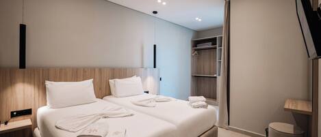 A modern hotel room with two beds, a wardrobe, a bedside table, and a trash bin.