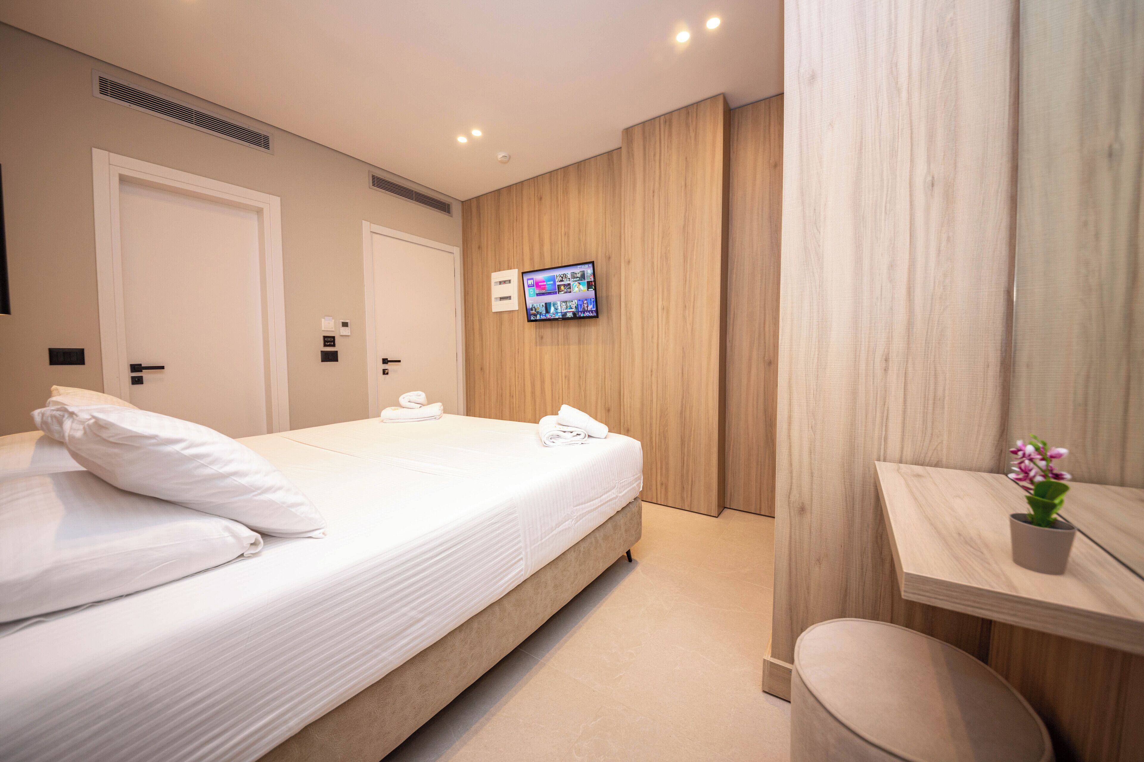 A hotel room with a large bed, a TV mounted on the wall, a small table with a plant, and a wooden panel wall.