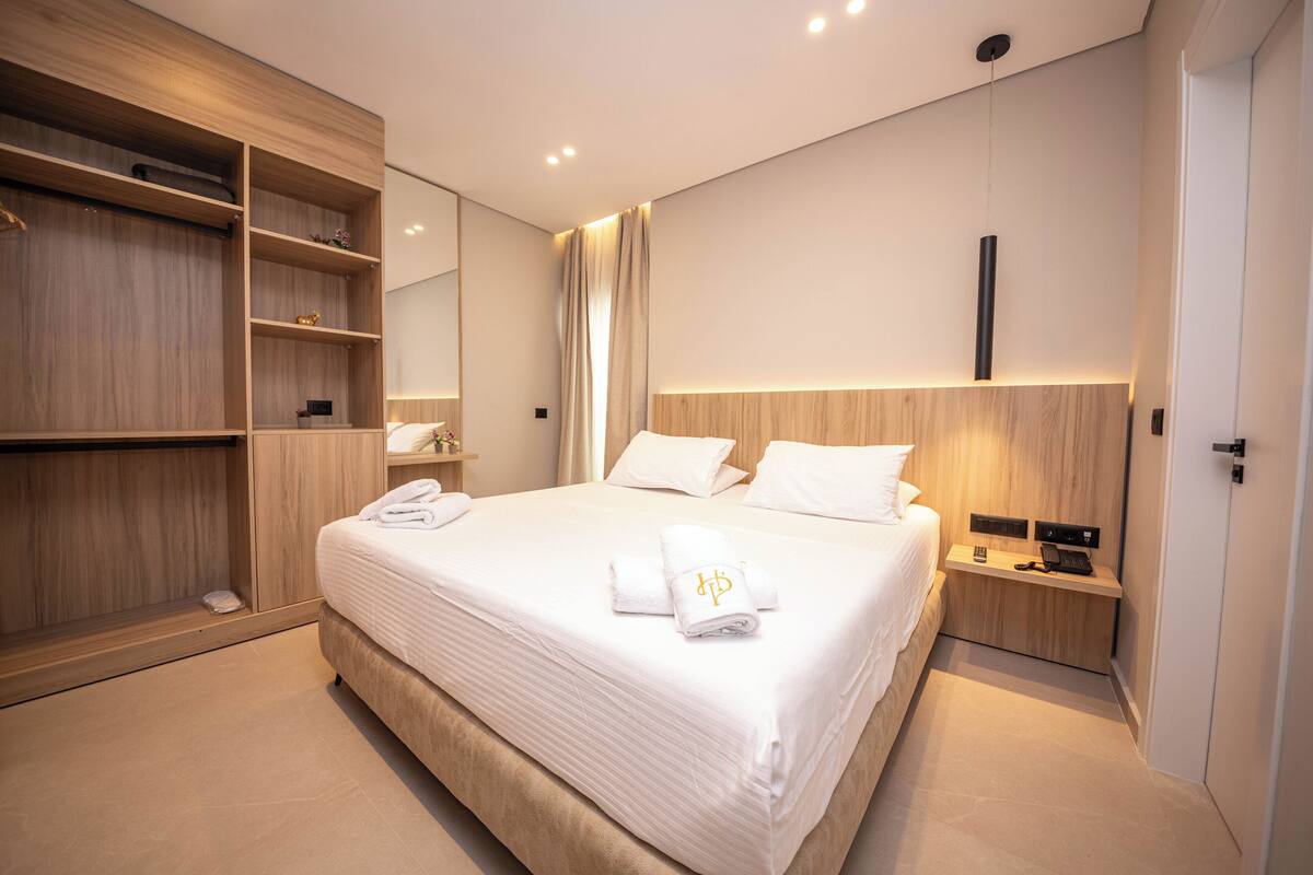Une chambre d’hôtel moderne avec un grand lit, une armoire en bois, une table de chevet avec une lampe et un miroir au mur.