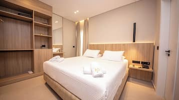 Una habitación de hotel moderna con una cama grande, un armario de madera, una mesita de noche con una lámpara y un espejo en la pared.