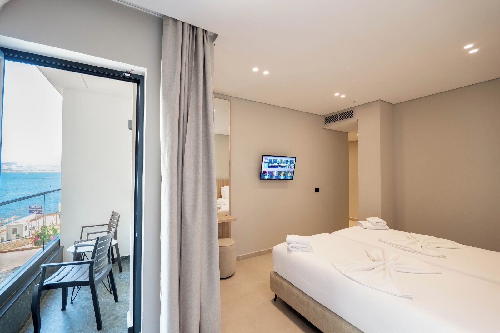 A hotel room with a balcony, a bed, a TV, and a small seating area.