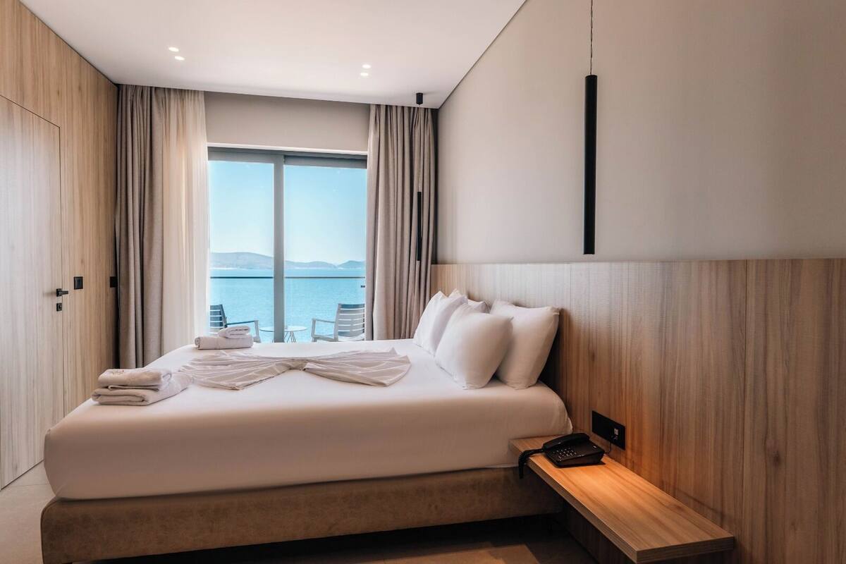 Une chambre d’hôtel moderne dotée d’un grand lit, d’une table de chevet avec un téléphone et offrant une vue sur la mer grâce à de grandes fenêtres.
