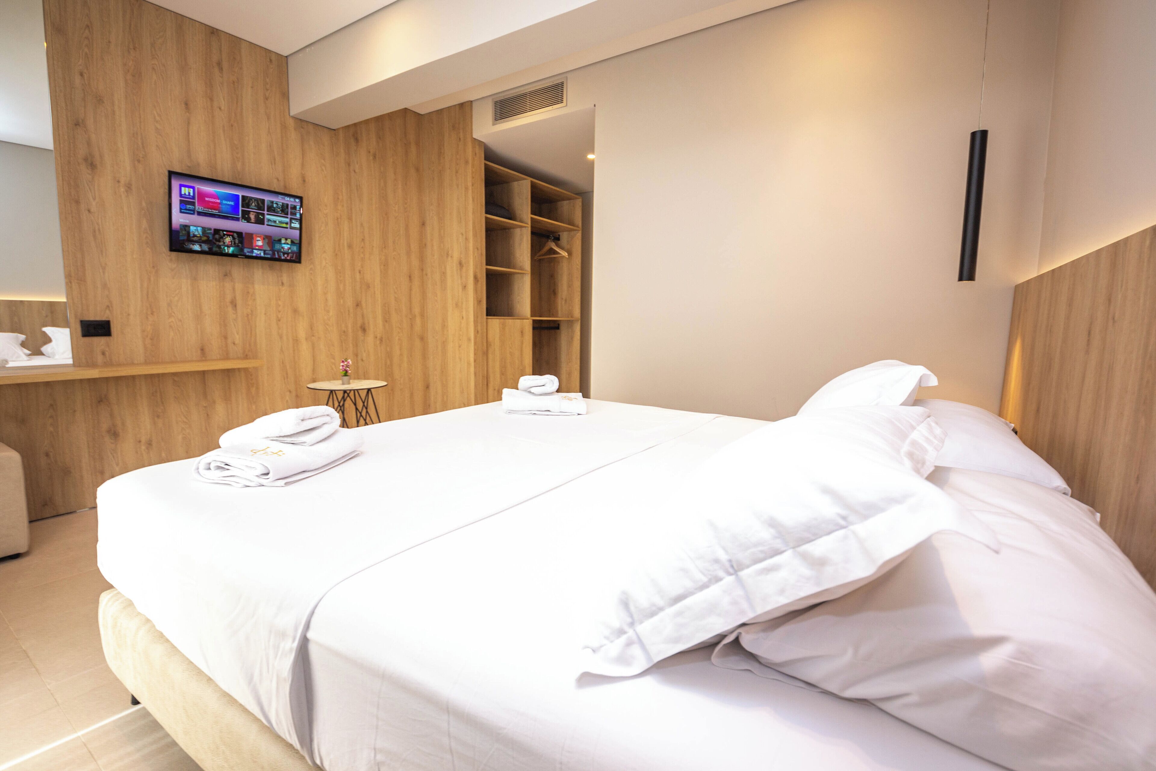 A modern hotel room with a neatly made bed, a television mounted on the wall, and a walk-in closet.