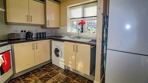 Eine kompakte Küche mit Waschmaschine, Kühlschrank und einem Fenster mit Jalousien.
