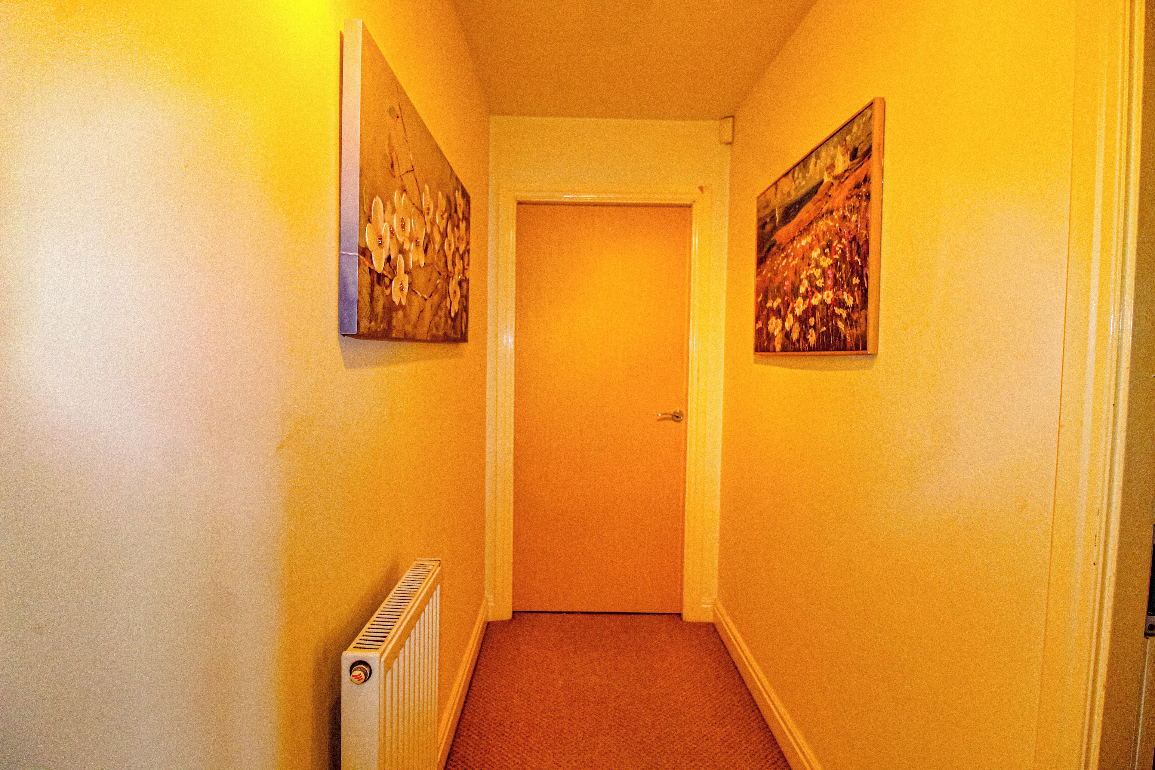 A narrow hallway with a radiator on the left and two framed pictures on the walls.