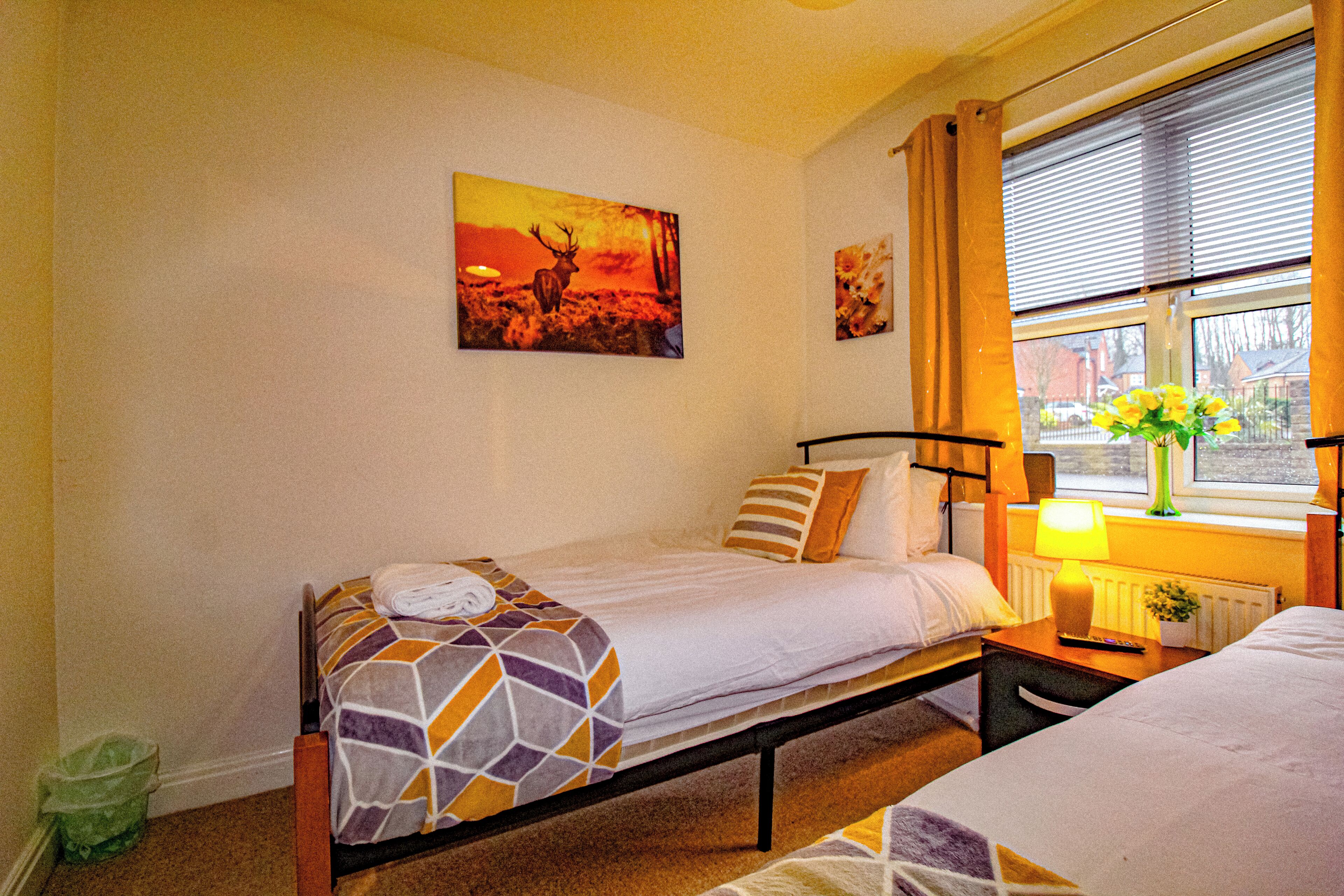 Ein Schlafzimmer mit zwei Einzelbetten, einem Fenster mit Vorhängen, einem Heizkörper und einem an der Wand hängenden Bild.