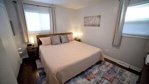 A bedroom with a large bed, two bedside tables, a nightstand, a rug, and a painting on the wall.