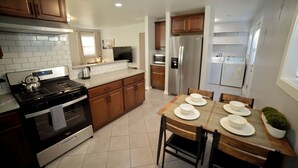A modern kitchen with wooden cabinets, stainless steel appliances, and a dining area with a table set for four.
