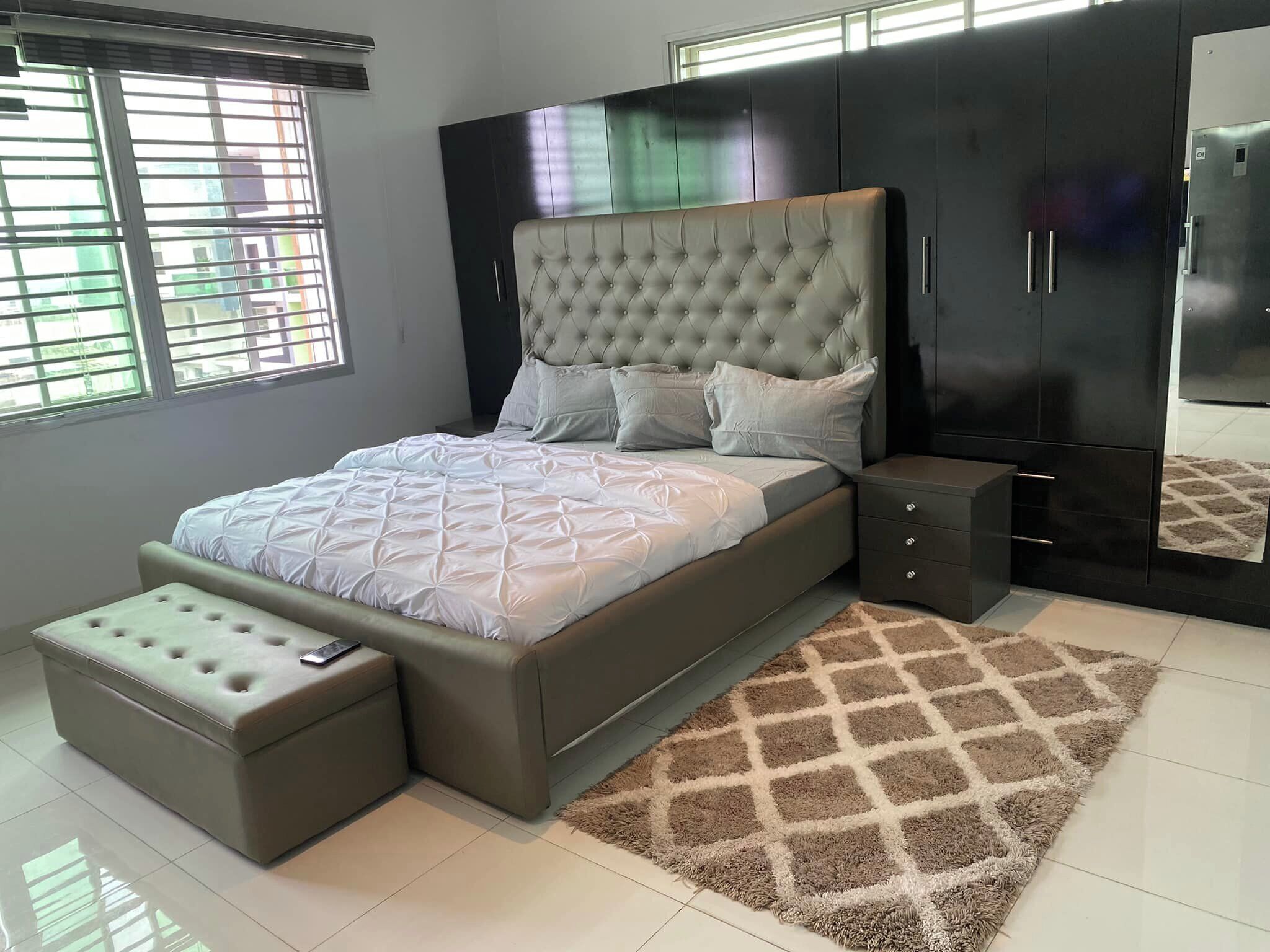 A modern bedroom with a large bed, a bedside table, a wardrobe, and a window with blinds.