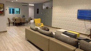 Een moderne woonkamer met een beige bank, een gele fauteuil, en een eethoek met een tafel en stoelen.