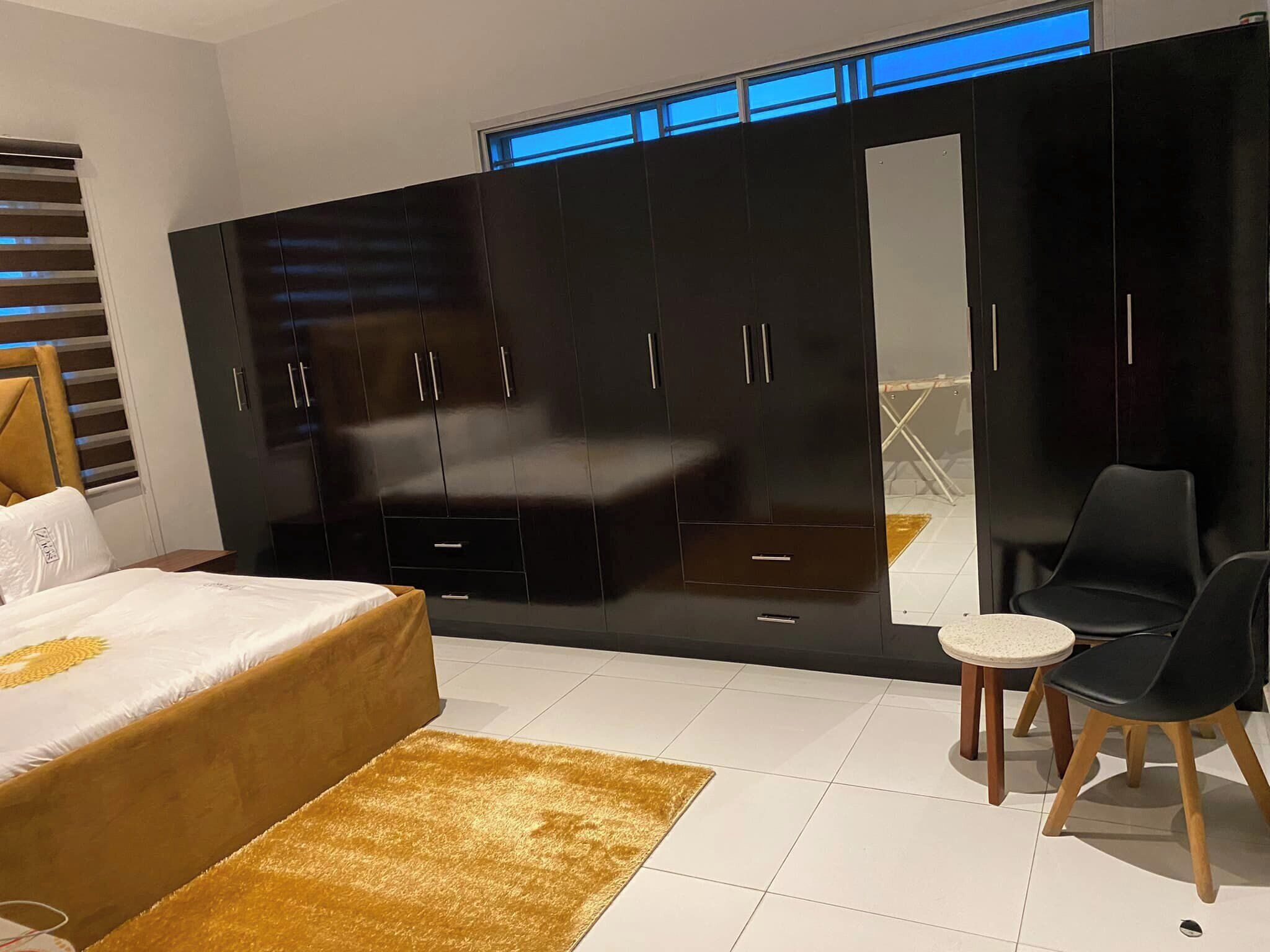 Un dormitorio moderno con un armario grande, una cama con detalles dorados y una pequeña mesa redonda con una silla.