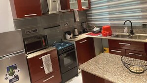Een kleine keuken met een koelkast, fornuis, oven, magnetron en een roestvrijstalen afzuigkap.