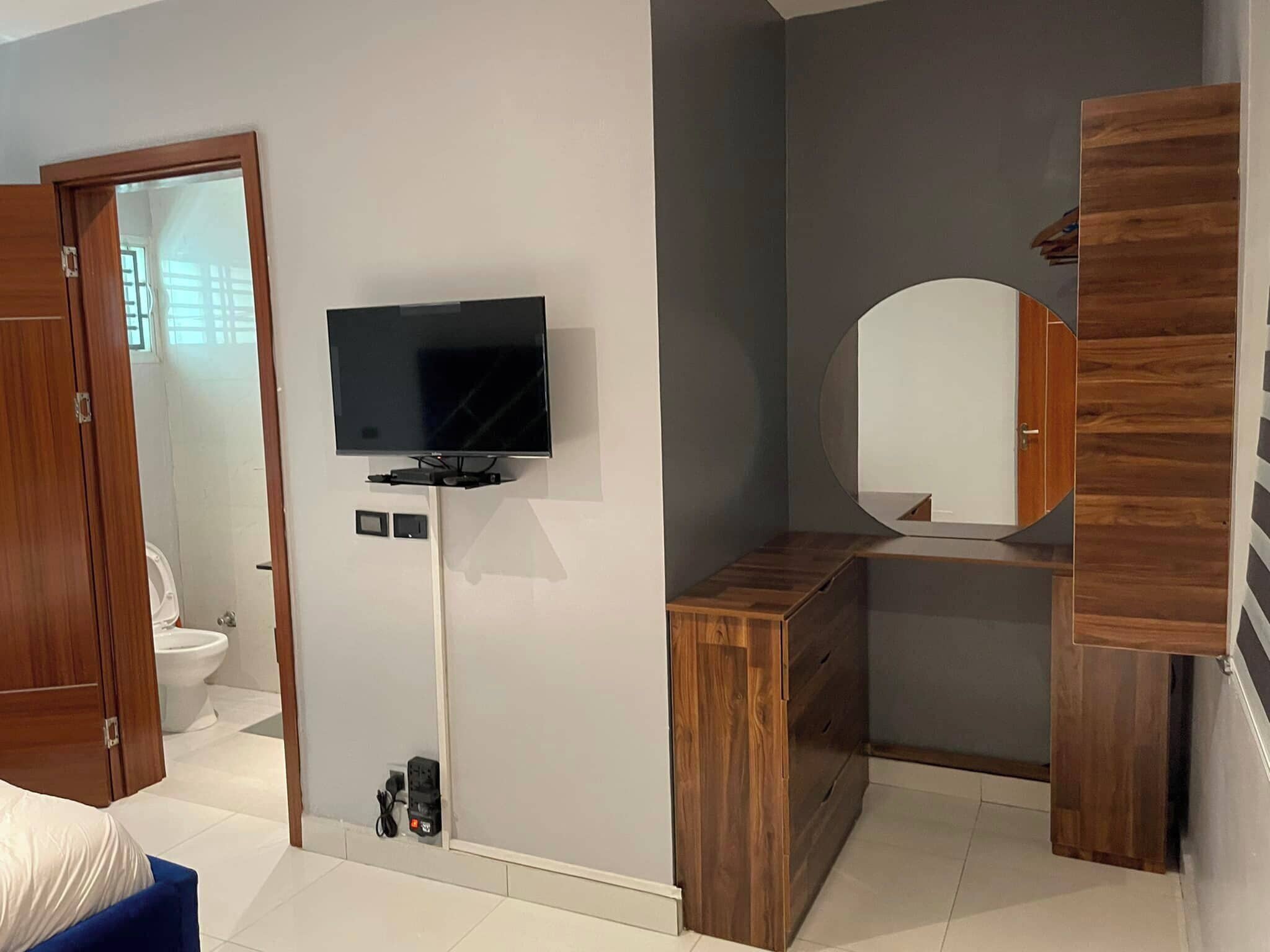 Un dormitorio moderno con un televisor montado en la pared, un armario de madera y un espejo.