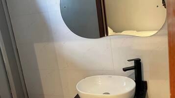 Un baño con un lavamanos blanco, un grifo negro y un espejo encima. Hay un inodoro con una tapa rosa y un gabinete de madera debajo del lavamanos.