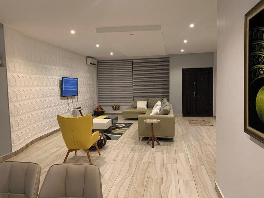 A modern living room with a sofa, armchairs, a television, and a patterned wall.