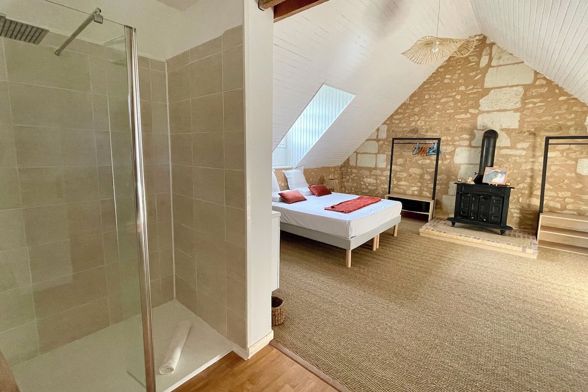 Ein Schlafzimmer mit schrägem Dach, einem Bett, einem kleinen schwarzen Heizgerät und einer Steinwand.