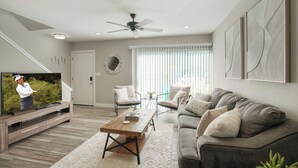 Een moderne woonkamer met een flatscreen-televisie, een plafondventilator en een groot raam met zonwering.