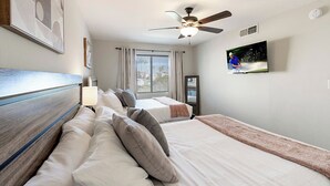 Een hotelkamer met twee bedden, een plafondventilator, een televisie en een raam met gordijnen.
