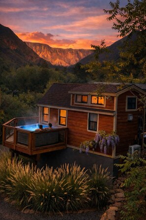 Una cabaña de madera con jacuzzi y terraza, rodeada de montañas y vegetación.