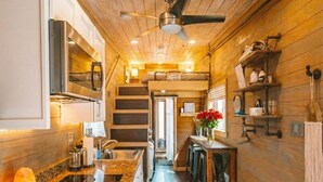 Une cuisine de taille modeste avec des murs en bois, un îlot central, un ventilateur de plafond et une porte visible donnant sur une autre pièce.