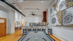 A pool table with a pool cue and balls, a ceiling fan, and a kitchen area with a bar.