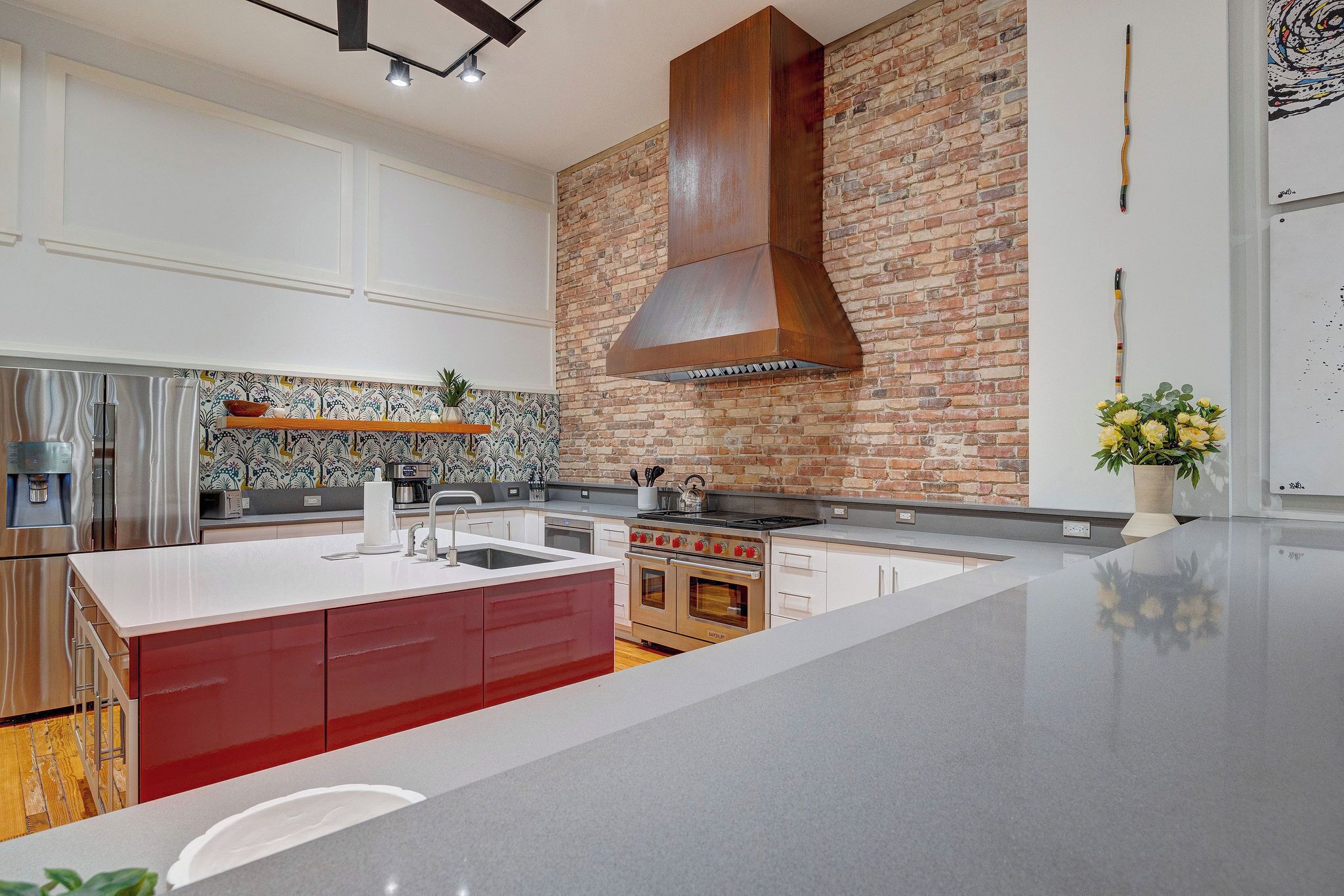 A modern kitchen with a large island, stainless steel appliances, and a brick accent wall.