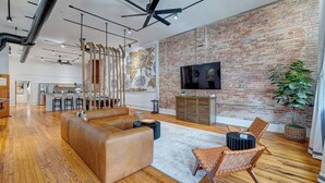 A spacious living area with a brick wall, a large sofa, a coffee table, and a TV mounted on the wall.