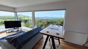 Una sala de estar moderna con un sofá, un televisor, una mesa con un cuenco de vidrio y ventanas amplias que ofrecen una vista panorámica.