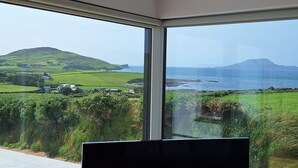 Una habitación con un amplio ventanal que ofrece vistas a un paisaje costero, incluyendo campos verdes, una colina y el mar.