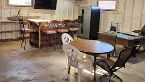 Une pièce rustique aménagée dans le style d’une grange, avec une table en bois, des chaises, une table de billard, un téléviseur et un réfrigérateur.
