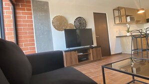 Ein modernes Wohnzimmer mit einer schwarzen Couch, einem Glastisch und einem Flachbildfernseher auf einem Holzständer.