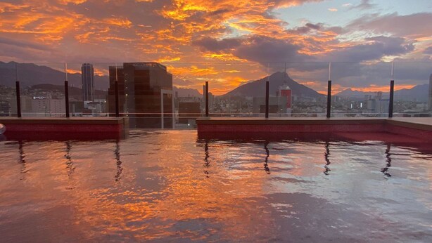 Ein Pool auf dem Dach mit Blick auf die Stadt und Berge im Sonnenuntergang.