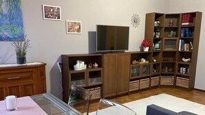 A living room with a glass-top dining table, a television, a bookshelf, and a white rug.