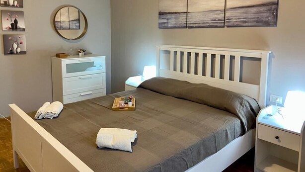A neatly arranged bedroom with a bed, bedside tables, a dresser, and wall art.