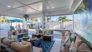 A sunlit indoor patio with wicker furniture, a pool, and a large mural. - Coral Cove (Fort Myers Beach)