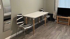 Un salon moderne comprenant une table à manger, deux chaises, un téléviseur posé sur un meuble, un canapé et un grand miroir.