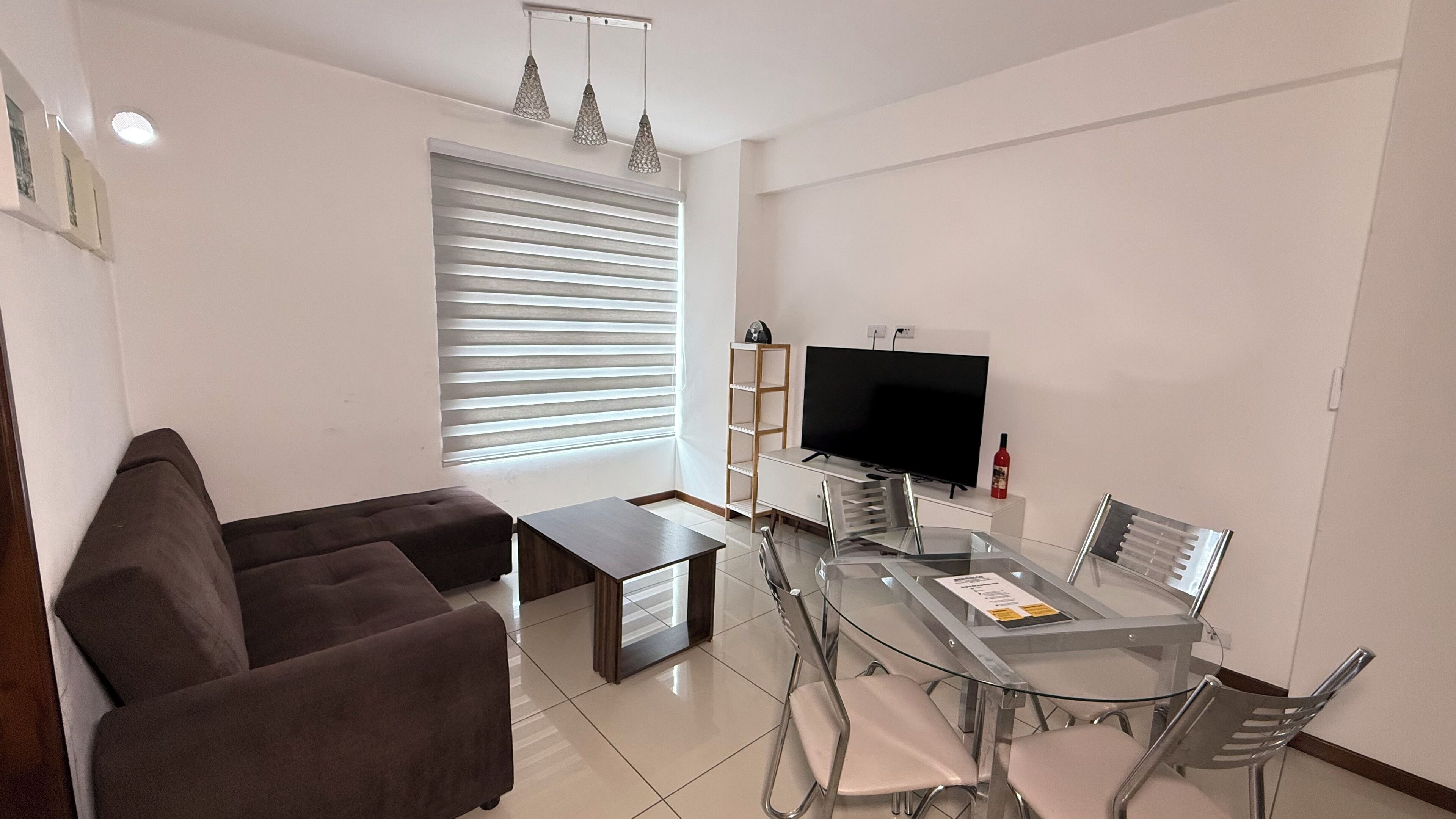 A modern living room with a sofa, a glass dining table with chairs, a TV, and a bookshelf.