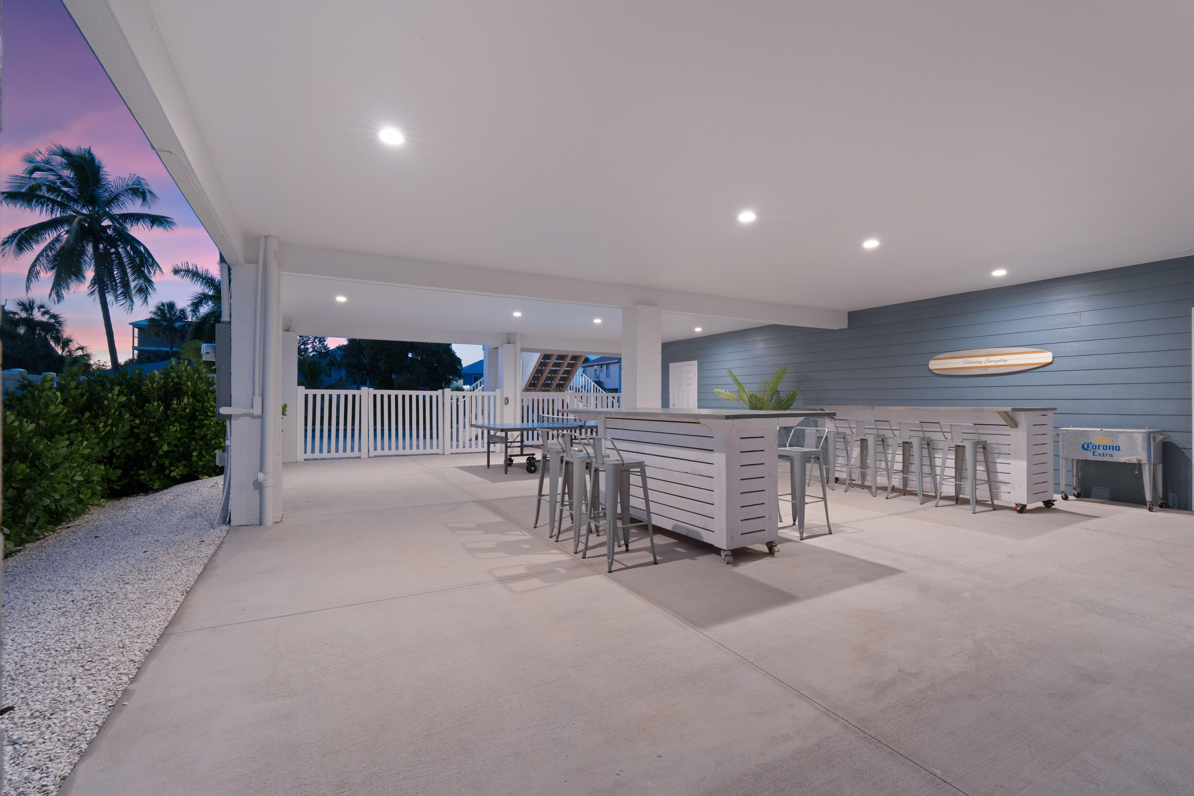An outdoor bar area with a counter, stools, and a Corona Extra cooler.