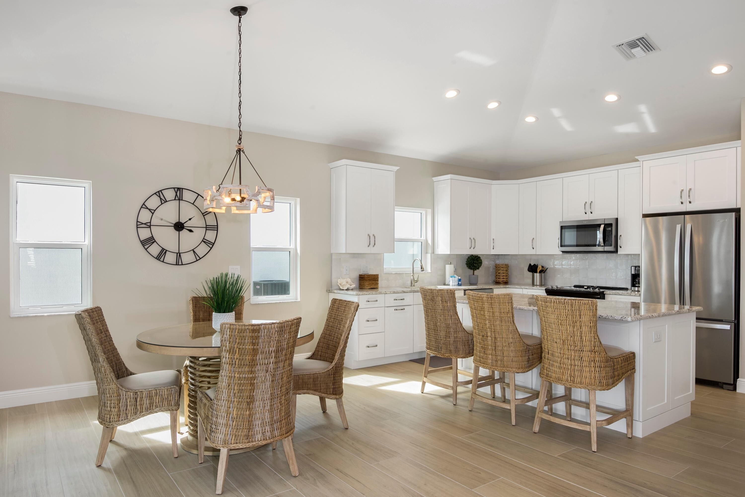 A modern kitchen with white cabinets, a stainless steel refrigerator, and a dining area with wicker chairs.