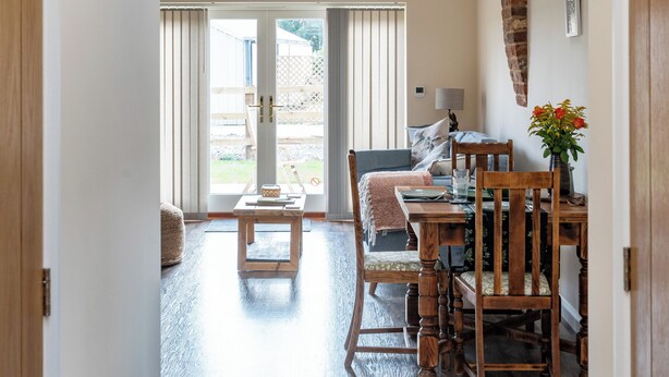 A spacious room with a high ceiling, wooden beams, a dining table with chairs, and a large window providing natural light.