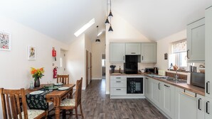 A modern kitchen with wooden flooring, white cabinets, and a dining area with a wooden table and chairs.