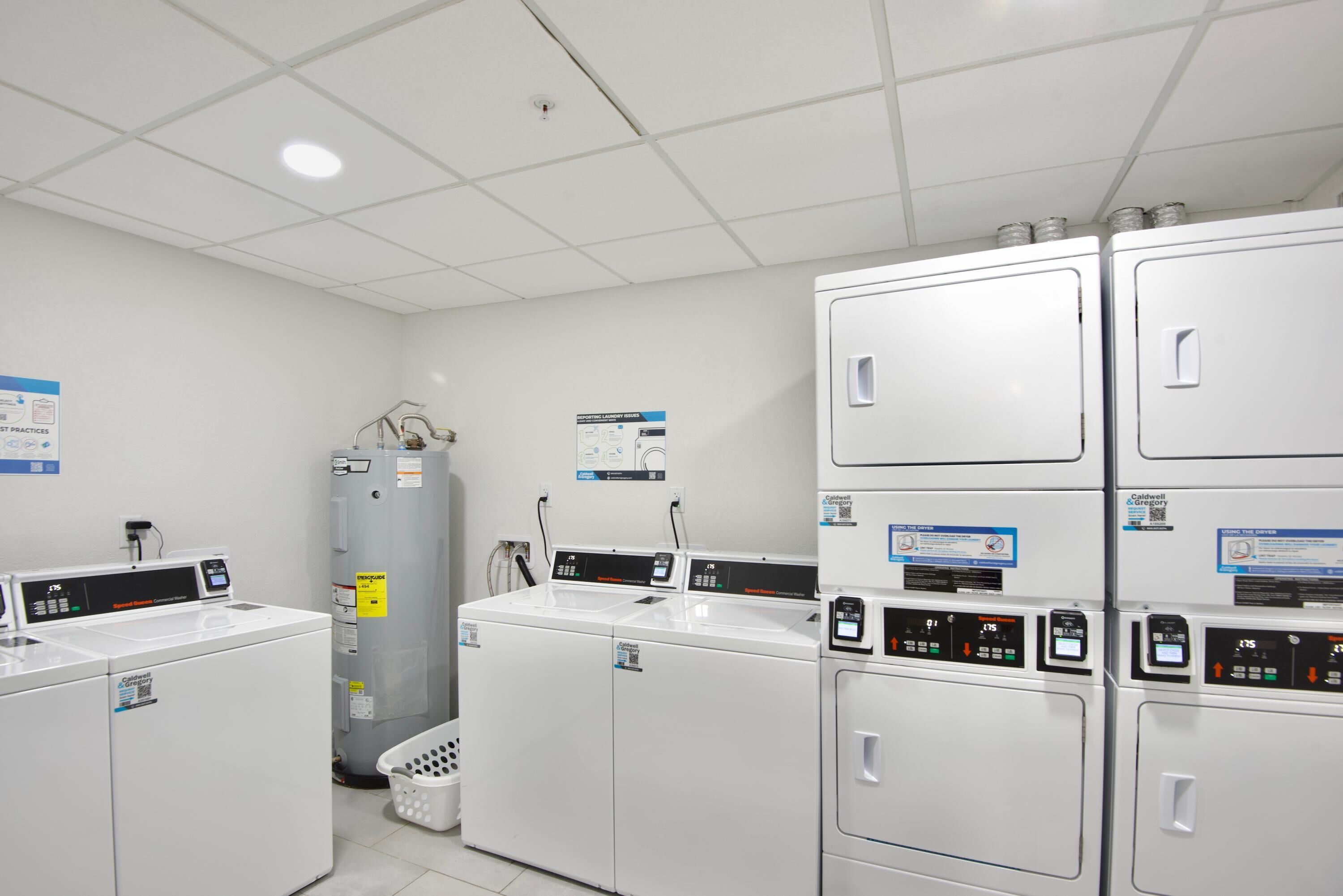 A laundry facility with multiple washing machines and dryers, a water heater, and a laundry basket.