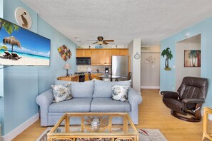 Una sala de estar con un sofá, una mesa de centro, un televisor, una zona de cocina y un sillón reclinable.