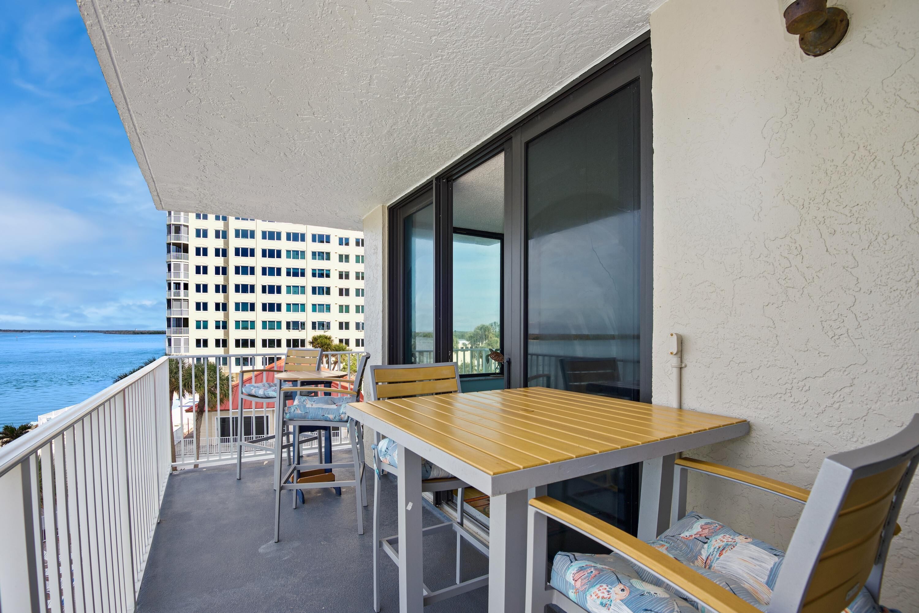 Ein Balkon mit Tisch und Stühlen, mit Blick auf ein Gewässer und ein Hochhaus.