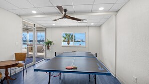 A ping pong table in a room with a ceiling fan, a window with a view, and a door leading outside. - Lovers Key Beach Club #303 (Fort Myers Beach)