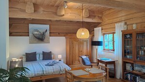 A cozy room with a bed, a dining table with chairs, a wooden cabinet with glass doors, and a hanging light fixture. - Quiet vacation apartment in a wooden house (on the edge of the forest) (Modautal)