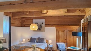 A cozy room with a bed, a dining table with chairs, a side table, a lamp, and a hanging light fixture. - Quiet vacation apartment in a wooden house (on the edge of the forest) (Modautal)