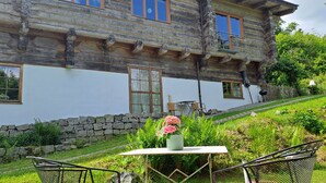 A rustic wooden house with a stone wall foundation, a balcony, and a table with chairs in the foreground. - Quiet vacation apartment in a wooden house (on the edge of the forest) (Modautal)