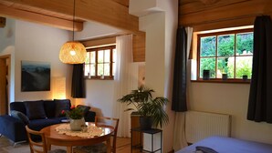 A cozy room with a wooden ceiling, a dining table with chairs, a sofa, a potted plant, and a bed with a white duvet. - Quiet vacation apartment in a wooden house (on the edge of the forest) (Modautal)
