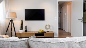 Une chambre à coucher moderne avec un lit, une lampe de chevet, un bureau avec une lampe, un téléviseur et un cactus.